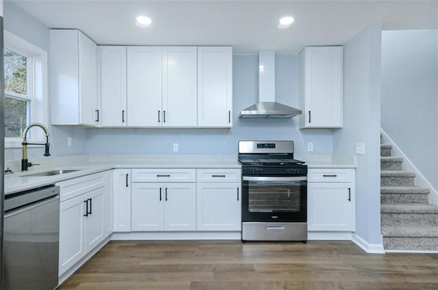 kitchen with appliances with stainless steel finishes, white cabinetry, and wall chimney range hood