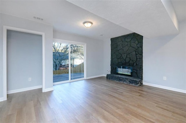 unfurnished living room with a stone fireplace, light hardwood / wood-style floors, and a textured ceiling