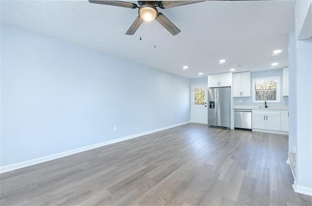 unfurnished living room with a textured ceiling, ceiling fan, light wood-type flooring, and sink