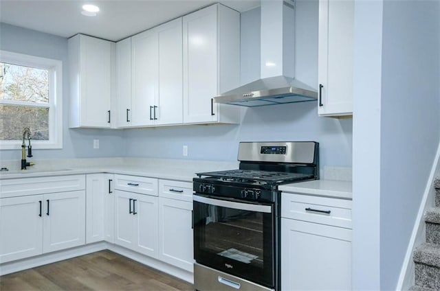 kitchen with wall chimney exhaust hood, gas range, sink, dark hardwood / wood-style floors, and white cabinetry