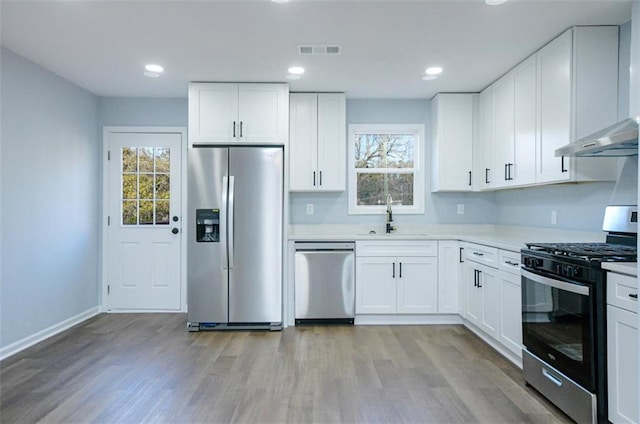 kitchen featuring white cabinetry, sink, a healthy amount of sunlight, exhaust hood, and appliances with stainless steel finishes