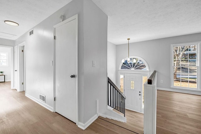 entrance foyer with visible vents, a textured ceiling, baseboards, and wood finished floors