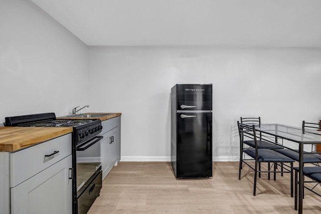 kitchen with butcher block countertops, a sink, baseboards, light wood-style floors, and black appliances