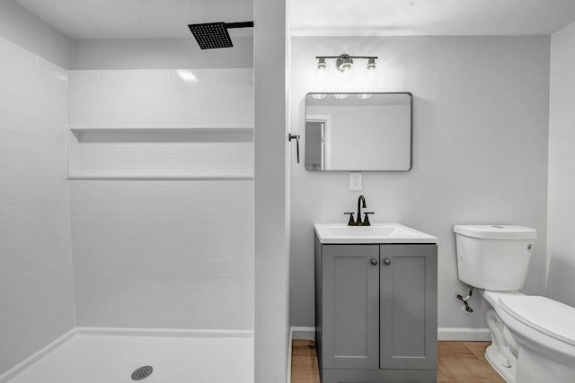 bathroom featuring toilet, vanity, wood finished floors, tiled shower, and baseboards