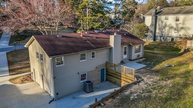 back of house featuring central AC, a shingled roof, and a chimney