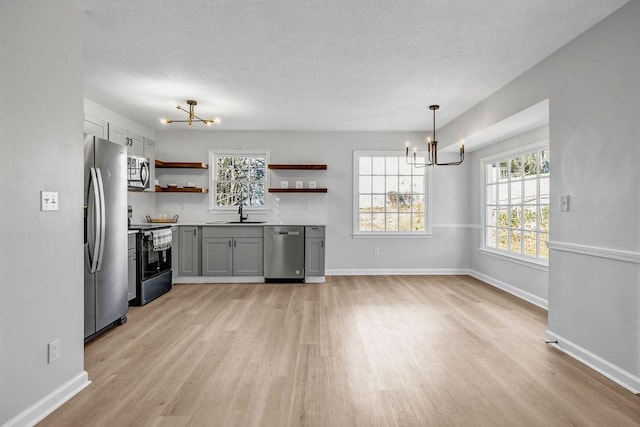 kitchen with stainless steel appliances, a sink, open shelves, and an inviting chandelier