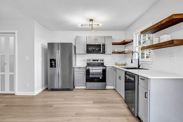 kitchen with open shelves, stainless steel appliances, gray cabinets, a sink, and light wood-type flooring