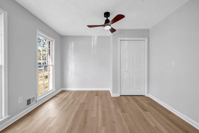 empty room with ceiling fan, light wood-style flooring, visible vents, and baseboards