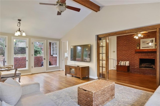 living room with beam ceiling, light hardwood / wood-style flooring, high vaulted ceiling, a fireplace, and ceiling fan with notable chandelier