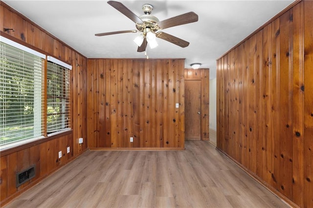 spare room featuring visible vents, ceiling fan, light wood-style flooring, and wooden walls