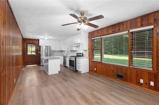 kitchen with under cabinet range hood, appliances with stainless steel finishes, visible vents, and wooden walls