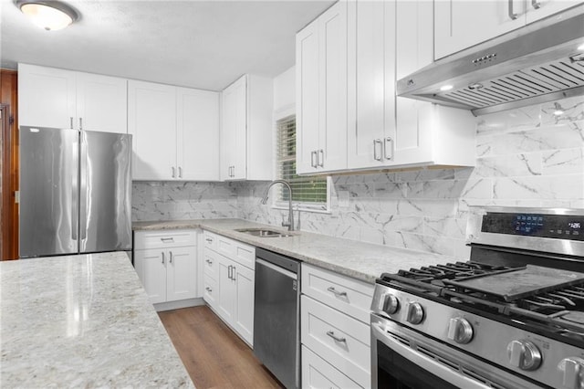 kitchen with appliances with stainless steel finishes, white cabinetry, tasteful backsplash, sink, and hardwood / wood-style flooring