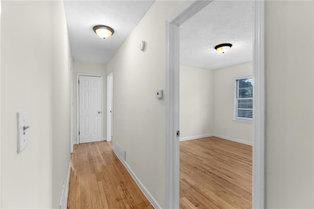 hallway featuring a textured ceiling, light wood finished floors, and baseboards