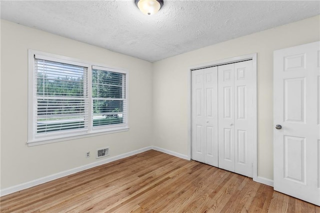 unfurnished bedroom with baseboards, visible vents, light wood-style flooring, a textured ceiling, and a closet