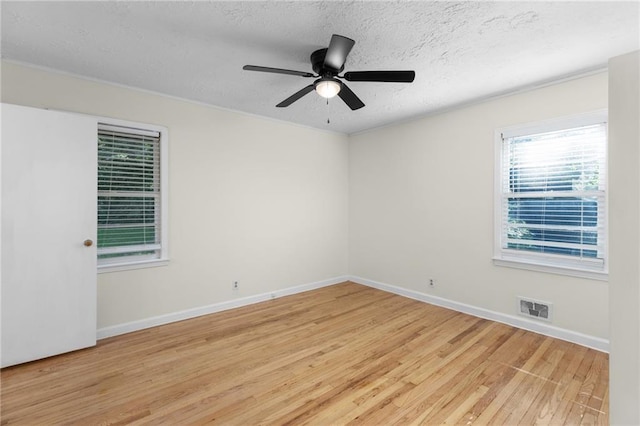 spare room featuring light wood-type flooring, visible vents, a textured ceiling, and baseboards