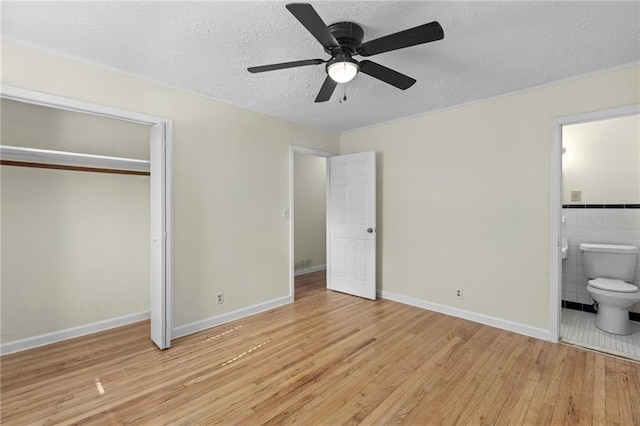 unfurnished bedroom with tile walls, a closet, ensuite bathroom, a textured ceiling, and wood finished floors