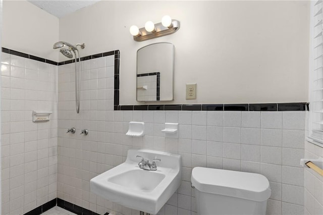 bathroom featuring tiled shower, a sink, tile walls, and toilet