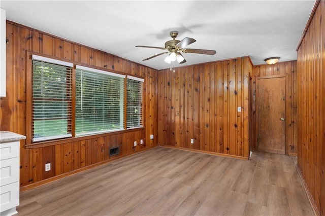 empty room featuring visible vents, baseboards, ceiling fan, light wood-type flooring, and wood walls