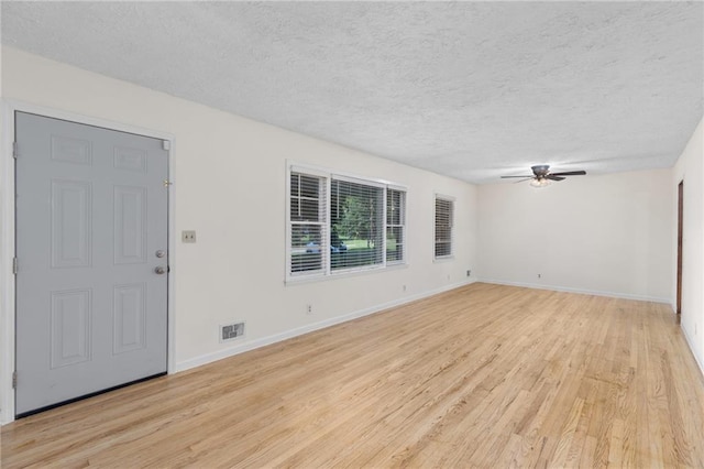 interior space with a textured ceiling, visible vents, baseboards, a ceiling fan, and light wood-type flooring