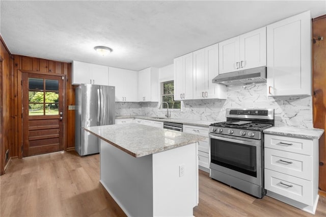 kitchen featuring under cabinet range hood, stainless steel appliances, a kitchen island, white cabinetry, and light wood-style floors