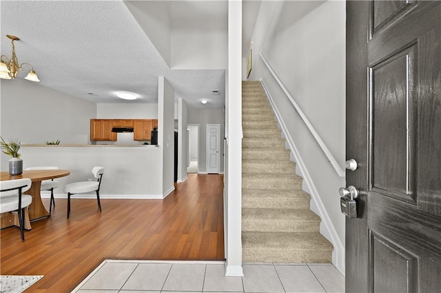 foyer featuring a textured ceiling, light tile patterned flooring, baseboards, stairs, and an inviting chandelier