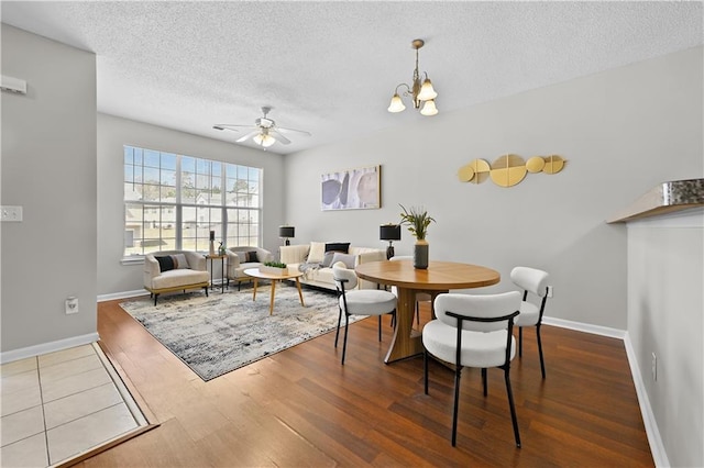 dining space featuring a textured ceiling, baseboards, wood finished floors, and ceiling fan with notable chandelier