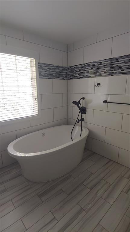 2477 Briar Valley Way, Dacula, GA 30019 - bathroom with wood tiled floor, a soaking tub, and tile walls