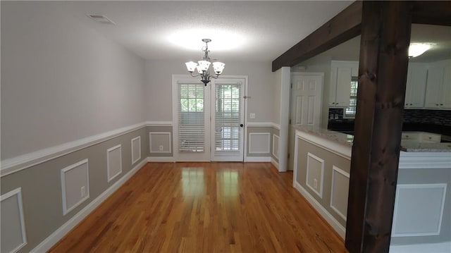 2477 Briar Valley Way, Dacula, GA 30019 - unfurnished dining area with an inviting chandelier, wainscoting, a decorative wall, light wood-type flooring, and visible vents