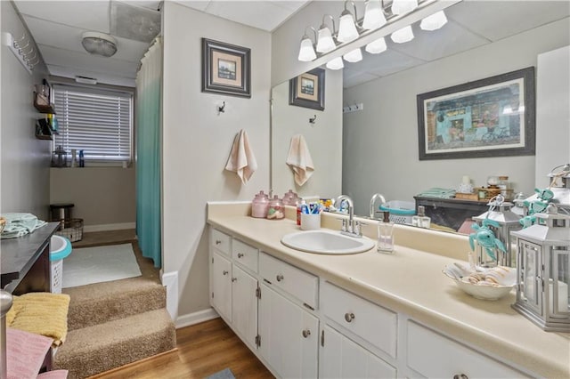 bathroom featuring a paneled ceiling, vanity, baseboards, and wood finished floors