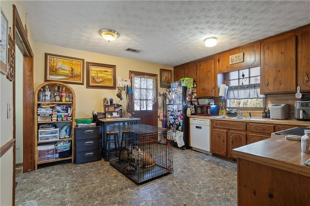 kitchen with white dishwasher, a sink, visible vents, and brown cabinets