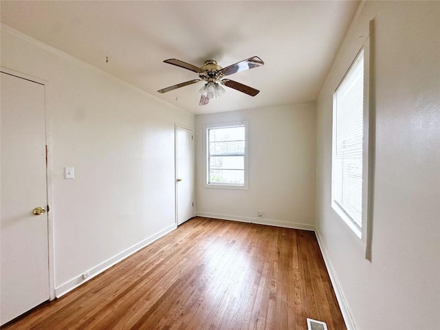 unfurnished room with ceiling fan, wood finished floors, visible vents, and baseboards