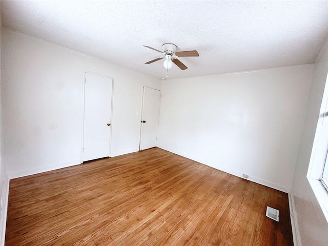 unfurnished bedroom featuring ceiling fan, light wood-style floors, visible vents, and a textured ceiling