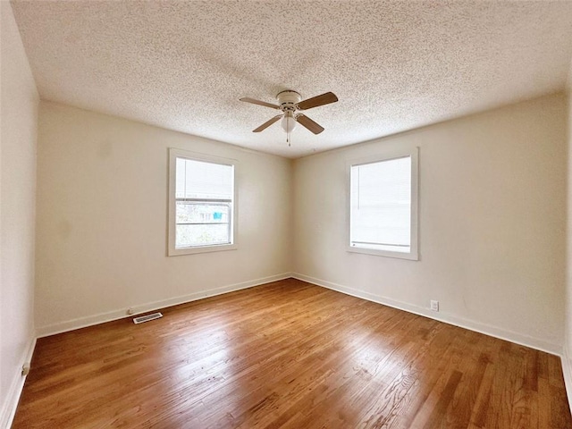 unfurnished room with visible vents, a ceiling fan, a textured ceiling, wood finished floors, and baseboards