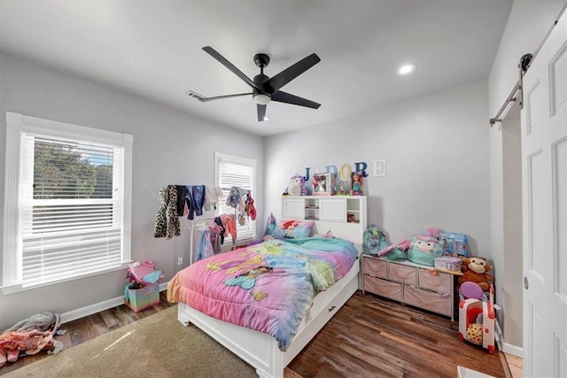 bedroom with dark wood-type flooring, ceiling fan, and a barn door