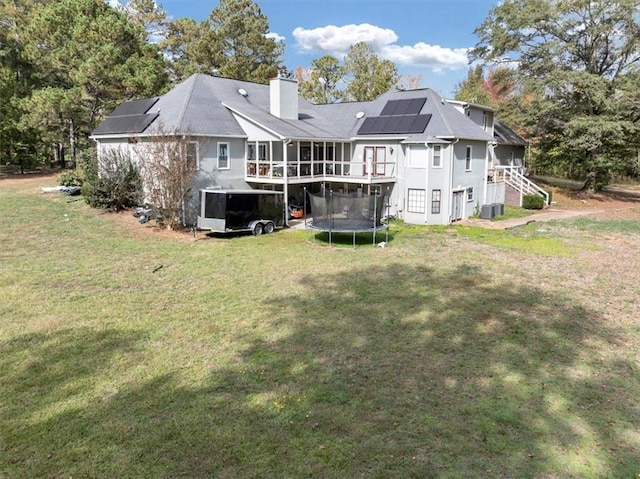 back of property featuring a yard, a trampoline, a deck, and solar panels