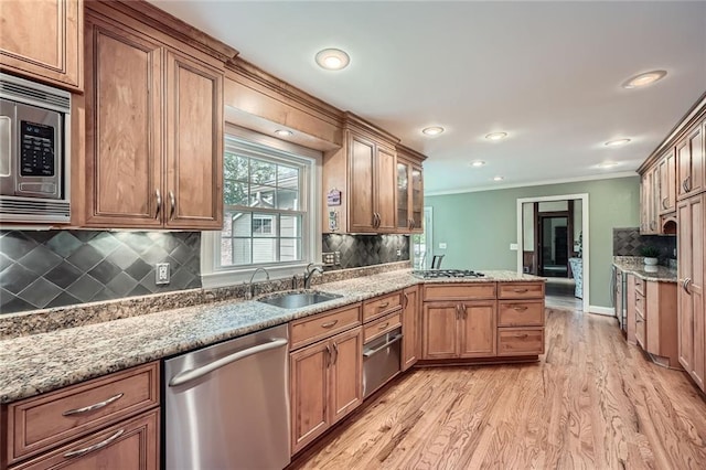kitchen with crown molding, light wood-style flooring, a sink, stainless steel appliances, and a peninsula