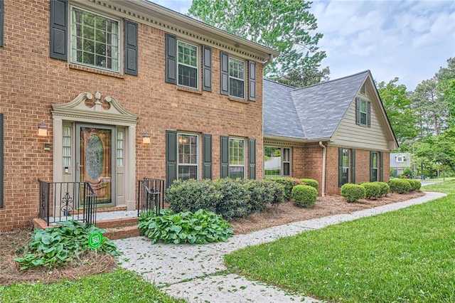 colonial inspired home with brick siding, a front lawn, and roof with shingles