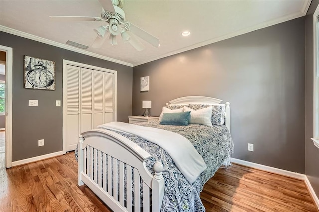 bedroom with baseboards, wood finished floors, crown molding, and a closet