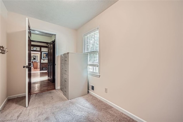 unfurnished room featuring a textured ceiling, visible vents, light colored carpet, and baseboards