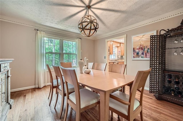 dining space with a textured ceiling, light wood-type flooring, ornamental molding, and baseboards