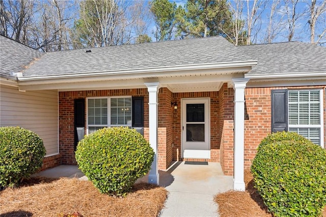 property entrance with a porch, brick siding, and roof with shingles