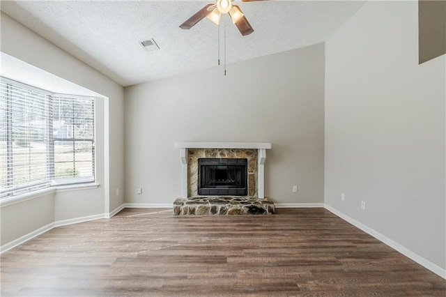 unfurnished living room with visible vents, wood finished floors, a textured ceiling, and a stone fireplace