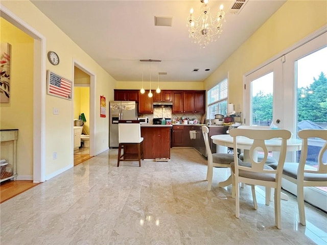 kitchen with stainless steel refrigerator with ice dispenser, light marble finish flooring, a chandelier, a kitchen island, and backsplash
