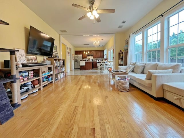 living room with light wood finished floors, healthy amount of natural light, ceiling fan, and a chandelier
