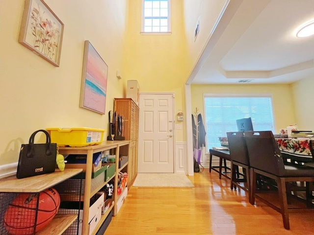 entryway with light wood-style floors, a wainscoted wall, and a tray ceiling