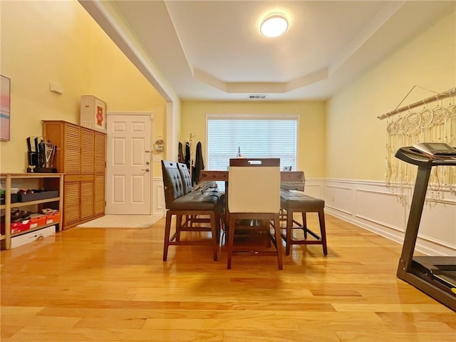 dining space featuring a tray ceiling, light wood-style floors, and wainscoting