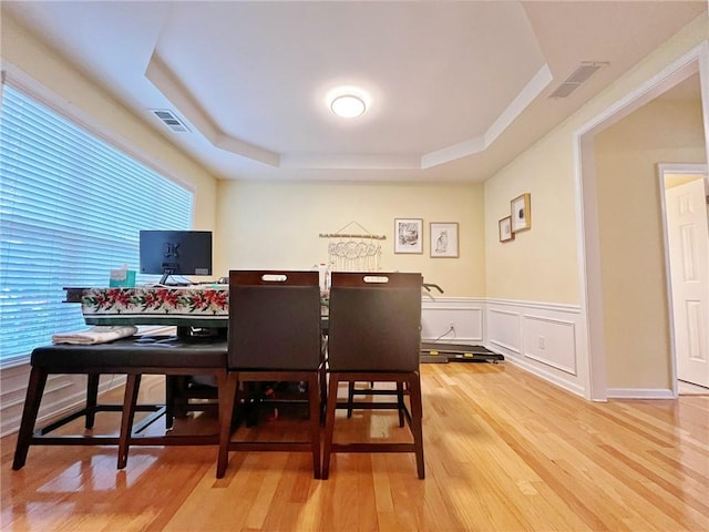 dining space featuring a raised ceiling, light wood finished floors, a desk, and a wainscoted wall