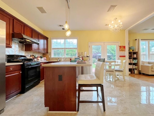 kitchen with black gas stove, under cabinet range hood, decorative backsplash, light countertops, and a breakfast bar