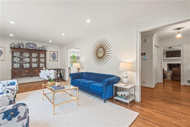 living room featuring wood finished floors, recessed lighting, crown molding, and a brick fireplace