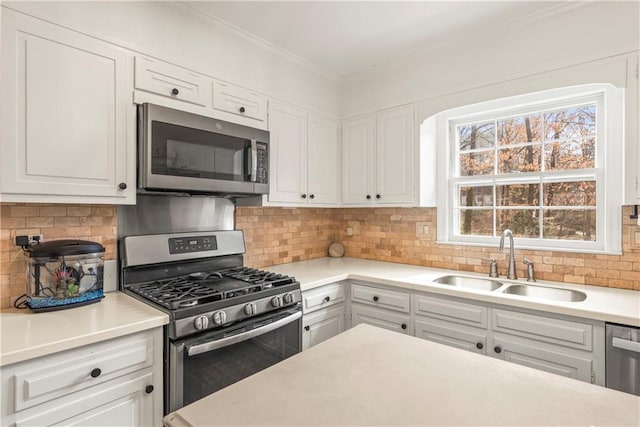 kitchen with light countertops, crown molding, stainless steel appliances, tasteful backsplash, and a sink